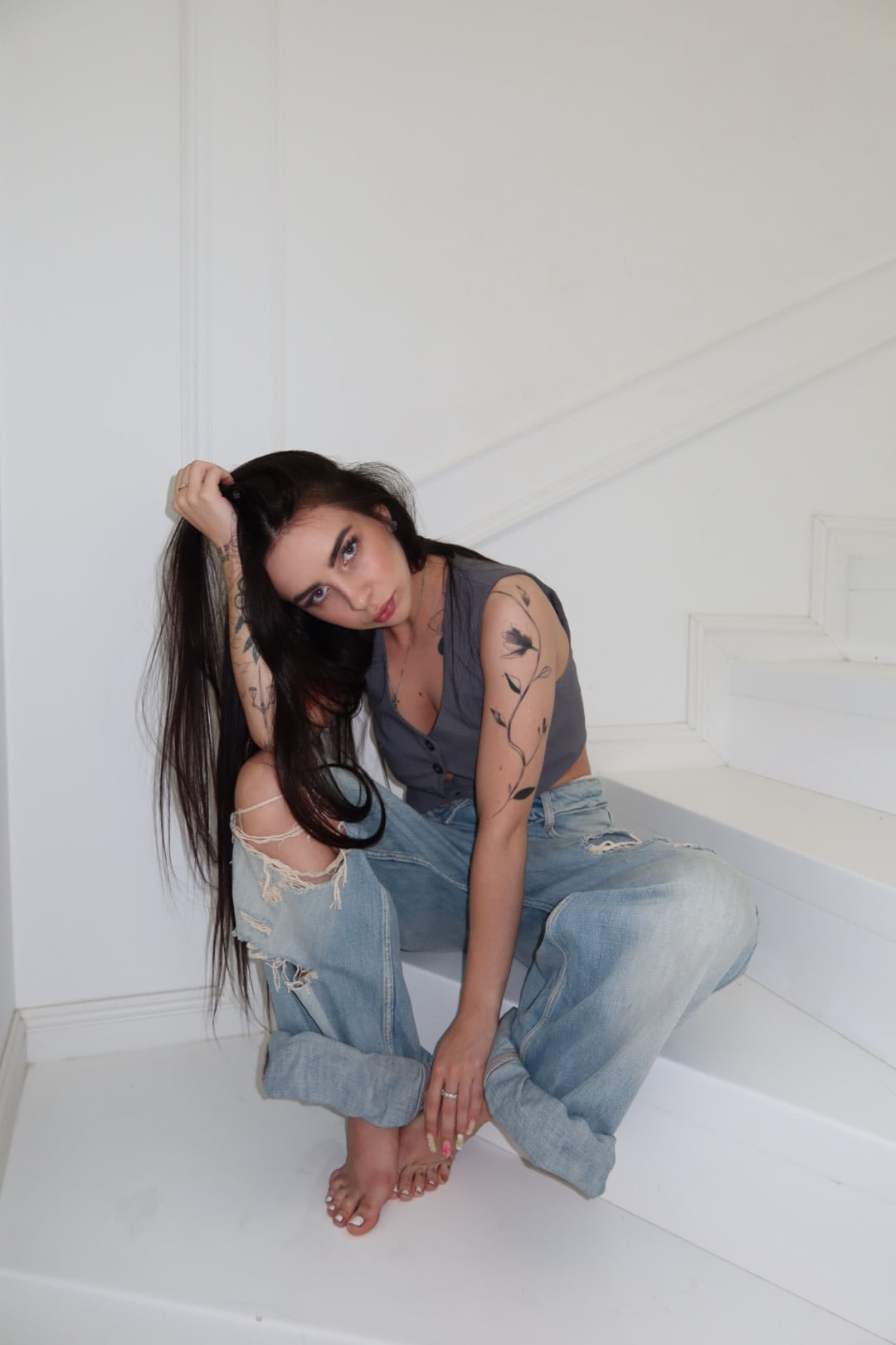 Lizaveta sitting on white stairs in a grey vest and light ripped jeans