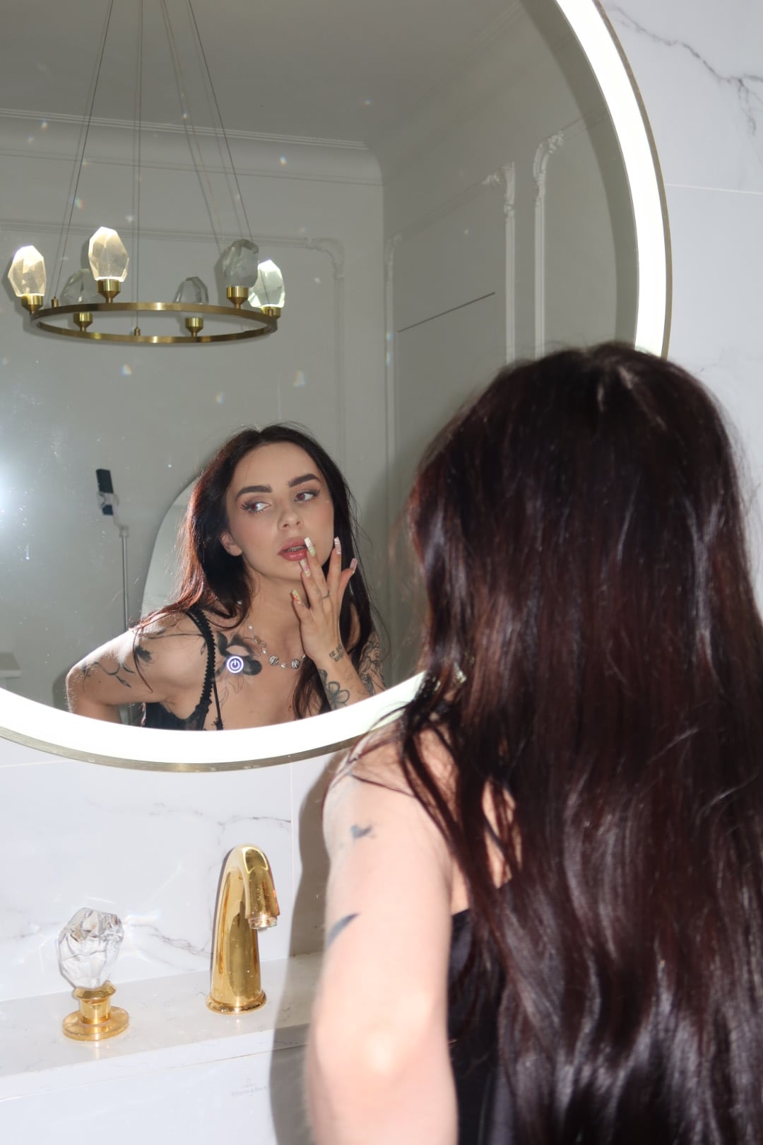 Lizaveta applying lip product, reflected in a round backlit mirror