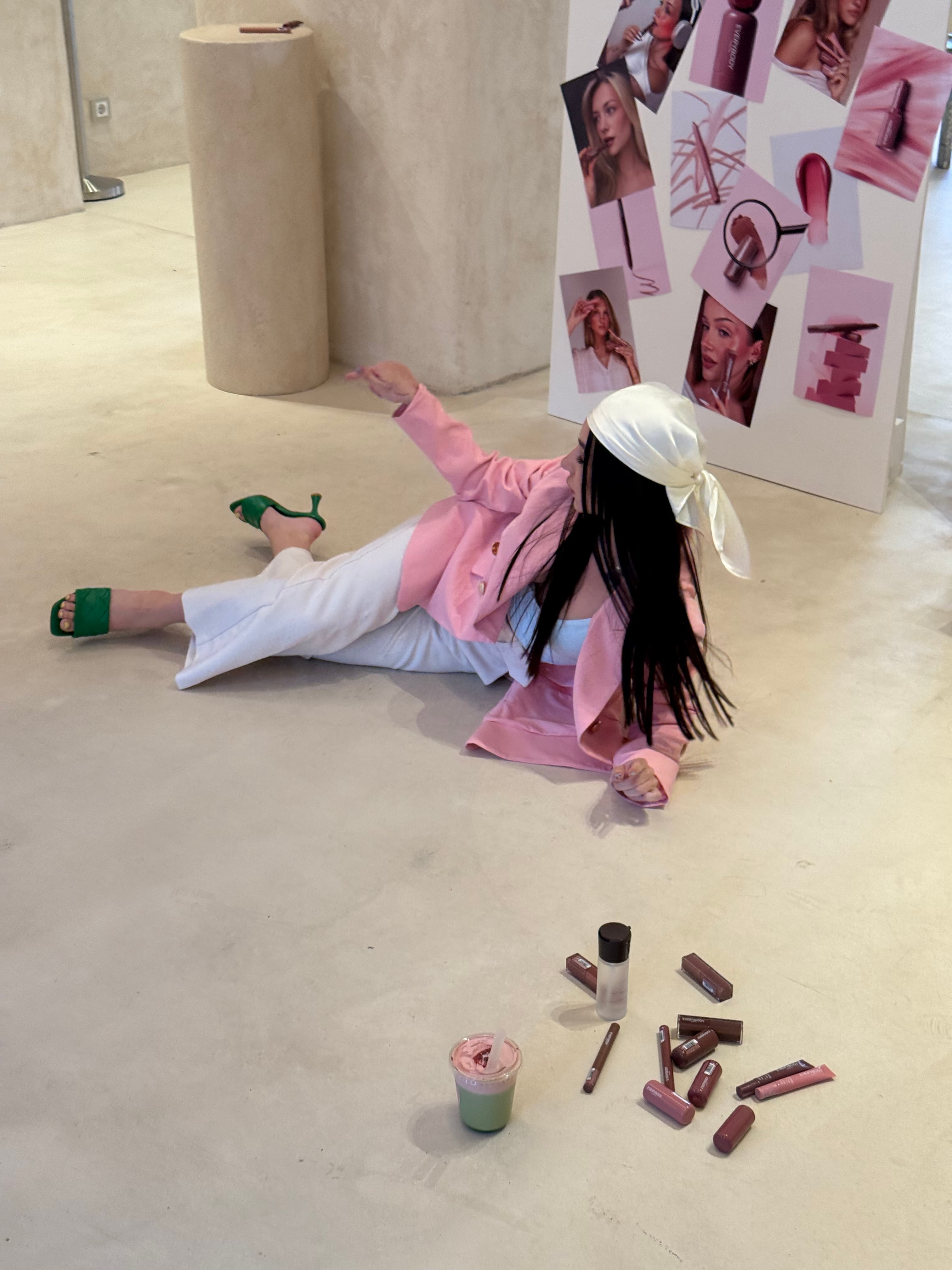 Lizaveta lying on a concrete floor in a pink blazer beside scattered Everybody London lip products